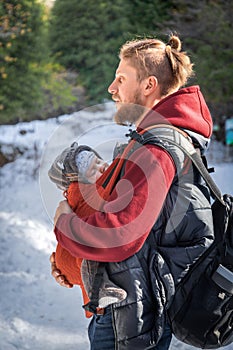 Young bearded babywearing father with his baby in sling winter walking outdoor