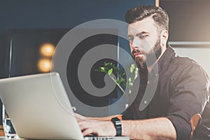 Young bearded businessman sitting in office at table and working on laptop. Man blogging, chatting, checking email.