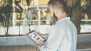 Young bearded businessman using tablet computer with graphs, diagrams and charts on screen.