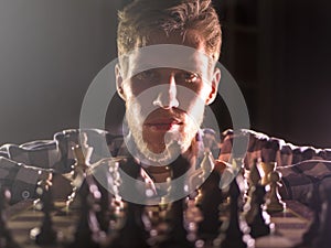 Young bearded chess grandmaster sitting and thinking on next move in dark room