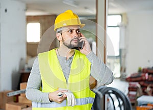 Young bearded civil engineer talking on phone at construction site