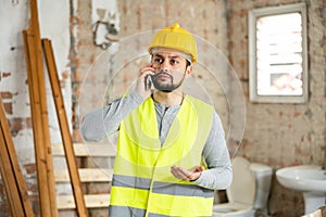 Young bearded civil engineer talking on phone at construction site