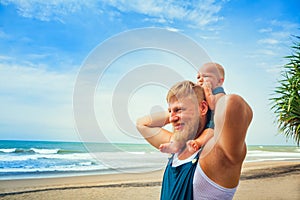 Young bearded father, funny baby son walk by tropical beach