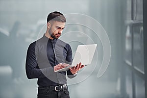 Young bearded guy in elegant clothes standing indoors against grey background