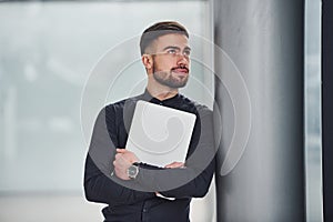 Young bearded guy in elegant clothes standing indoors against grey background