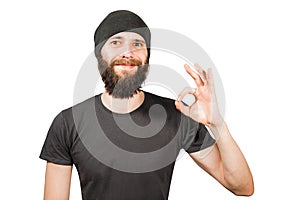 Young bearded guy in hat, smiles and show ok. Isolated on white background