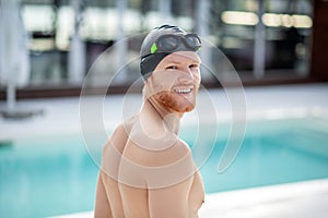 Young bearded guy in swimming cap standing near pool