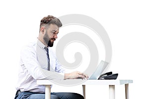 Young, bearded guy on worktable, using a laptop, looking at the screen. a man working, studying or surfing the web