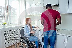 Young bearded handicapped redhaired ginger wife in wheelchair and her african american husband at kichen