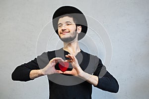 Young bearded hipster dressed in black, holding red heart in hands. Valentines day background.