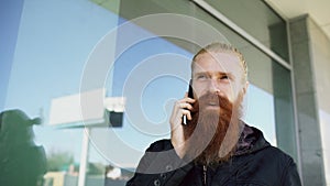 Young bearded hipster man concentrated talking on phone on citystreet and have conversation near office building