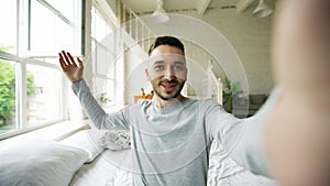 Young bearded man using tablet computer having video chat sitting in bed at home