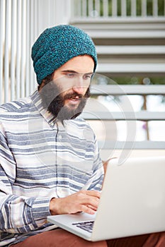 Young bearded hipster student using computer outdoors