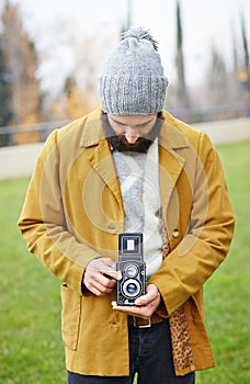 Young bearded hipster taking photo with TLR camera