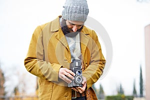 Young bearded hipster taking photo with TLR camera