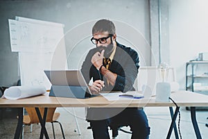 Young bearded male architect wearing eye glasses working on a digital tablet dock at his desk. Professional experienced