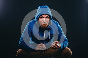 Young bearded male bully sits on black background