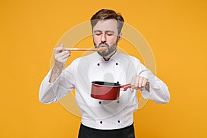 Young bearded male chef cook or baker man in white uniform shirt posing isolated on yellow background in studio. Cooking