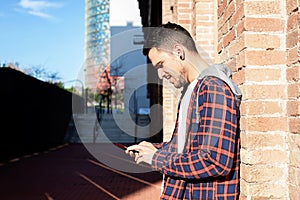 Young bearded male leaning on a bricked wall while using a smartphone