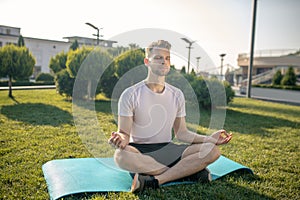 Young bearded male sitting in lotus pose outside, hands in Gyan mudra