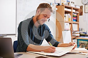 Young bearded male teacher at desk marking studentsÃ¯Â¿Â½ work photo