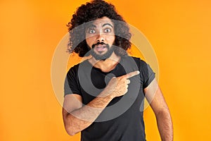 Young bearded male with trendy hairdo points with index finger aside, show something