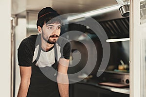 Young Bearded Man in Apron Standing in Food Truck.