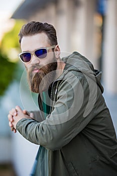 Young bearded man with a beard and mustache with glasses posing on the street, outdoor portrait