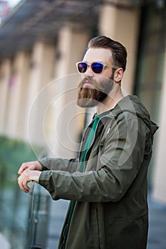 Young bearded man with a beard and mustache with glasses posing on the street, outdoor portrait
