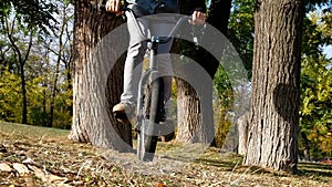 Young bearded man bmx rider in earphones riding through trees in park