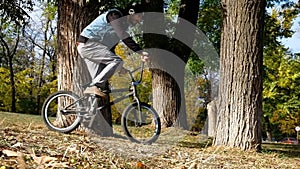 Young bearded man bmx rider in earphones riding through trees in park