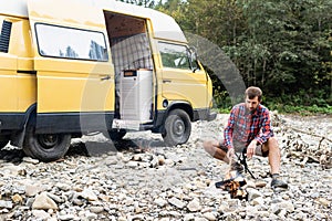 Young bearded man burning campfire by camper van in the woods