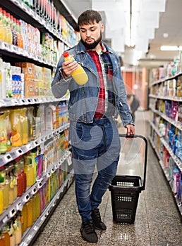 Young bearded man choosing bottled fresh juices in grocery section at supermarket