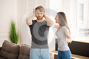 Young bearded man closing his ears while his wife shouting