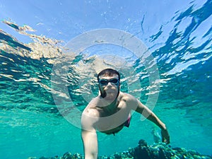 Young bearded man diving in a blue clean water