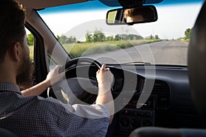 Young bearded man driving a car on old highway. Both hands holding a steering wheel