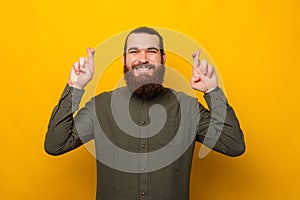 Young bearded man with exhilarated face is crossing fingers for a wish.