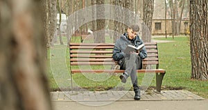 Young bearded man finishes reading a book in autumn park, gets up from bench and leaving elsewhere. Reading concept