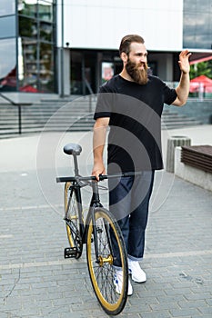 Young hipster bearded man with fixed gear bike waving hand on city street photo