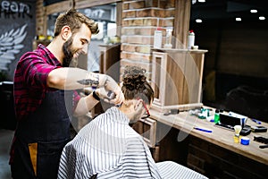 Young bearded man getting haircut by hairdresser while sitting in chair at barbershop