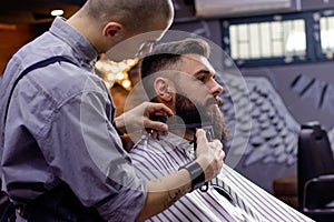 Young bearded man getting shaved in barber shop.