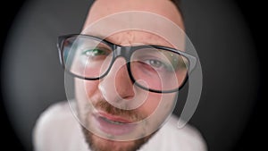 A young, bearded man with glasses looking in peephole. Distrust look for something.