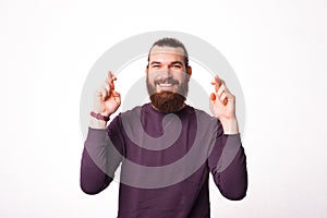 Young bearded man holding his hands with fingers crossed hoping that his dream will come true