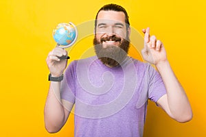 Young bearded man is holding a small globe and crossing fingers. photo