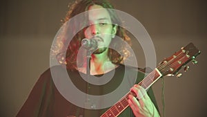 A young bearded man with long hair playing a song by the guitar at his performance