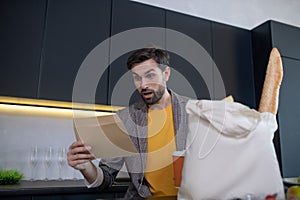 Young bearded man looking shocked lookig at the bill from the store photo