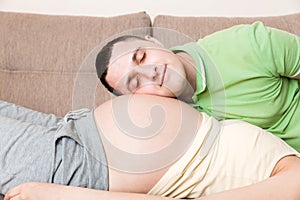 Young bearded man putting his ear close to his pregnant wifes abdomen and Listening it