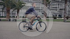 Young bearded man is riding bicycle in park area in summer day, side view