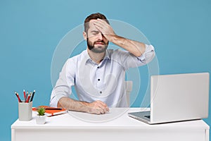 Young bearded man in shirt sit work at desk with pc laptop isolated on pastel blue background. Achievement business photo