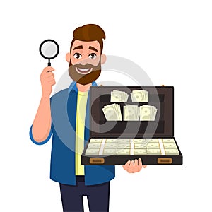 Young bearded man showing/holding magnifying glass and brief case full of money/cash/currency bank notes. Search, find, discovery.